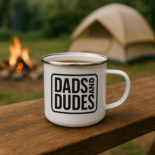 Dads and Dudes Enamel Logo Mug on a bench in front of campsite.